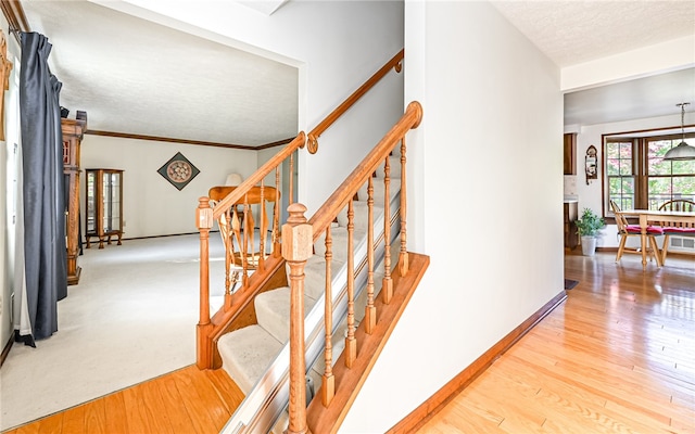 staircase with hardwood / wood-style floors, crown molding, and a textured ceiling