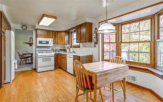 kitchen with white appliances, light wood-type flooring, sink, and pendant lighting