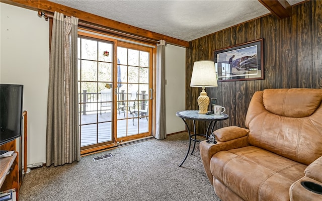 sitting room with wood walls, carpet, a textured ceiling, and beamed ceiling