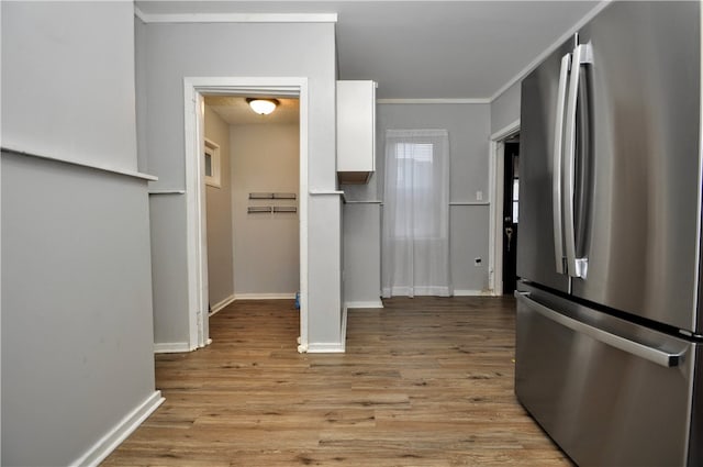 kitchen with white cabinetry, stainless steel fridge, light wood-type flooring, and ornamental molding