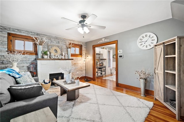 living room with a brick fireplace, hardwood / wood-style flooring, vaulted ceiling, and ceiling fan