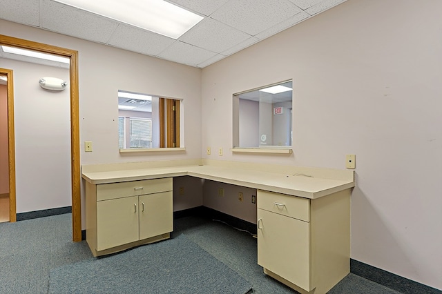 unfurnished office with a drop ceiling, built in desk, and dark carpet