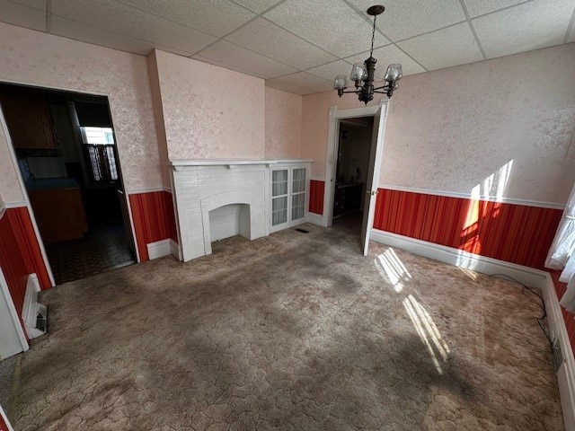 unfurnished living room with a drop ceiling, a notable chandelier, and carpet floors