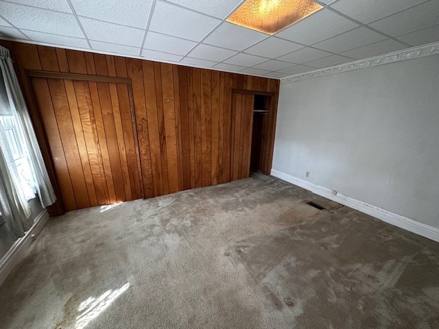 unfurnished bedroom with a drop ceiling, carpet floors, a closet, and wood walls