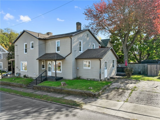 view of front facade featuring roof with shingles, a chimney, a front yard, and fence