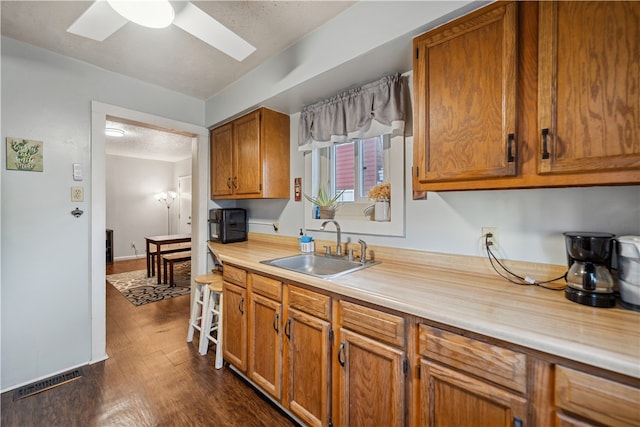 kitchen featuring brown cabinetry, dark wood-style flooring, light countertops, and a sink