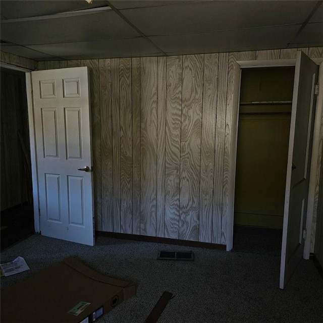 interior space featuring a closet, a paneled ceiling, carpet flooring, and wood walls