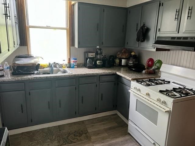 kitchen featuring exhaust hood, white gas range oven, gray cabinetry, and dark hardwood / wood-style flooring