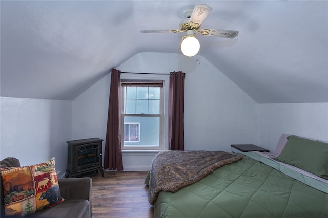 bedroom with dark wood-type flooring, ceiling fan, a wood stove, and vaulted ceiling