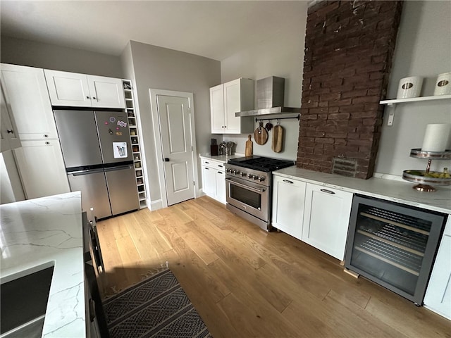 kitchen with beverage cooler, appliances with stainless steel finishes, light hardwood / wood-style floors, wall chimney exhaust hood, and white cabinets