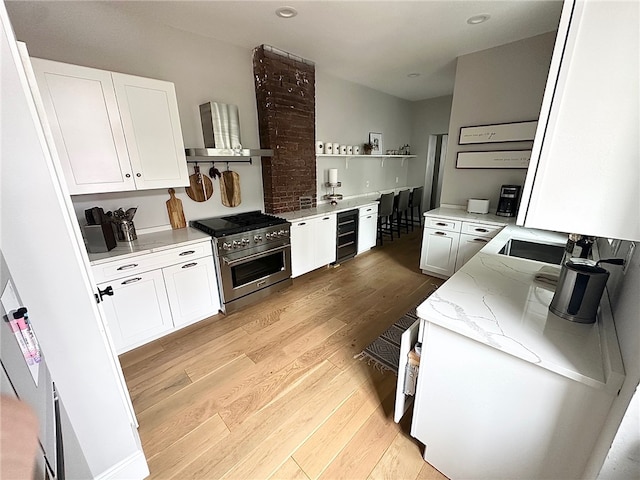 kitchen with wall chimney range hood, white cabinetry, light hardwood / wood-style floors, stainless steel stove, and wine cooler