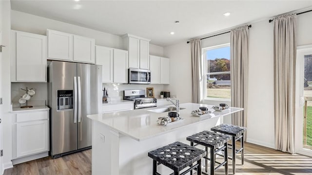 kitchen with white cabinetry, sink, light hardwood / wood-style flooring, a kitchen island with sink, and appliances with stainless steel finishes