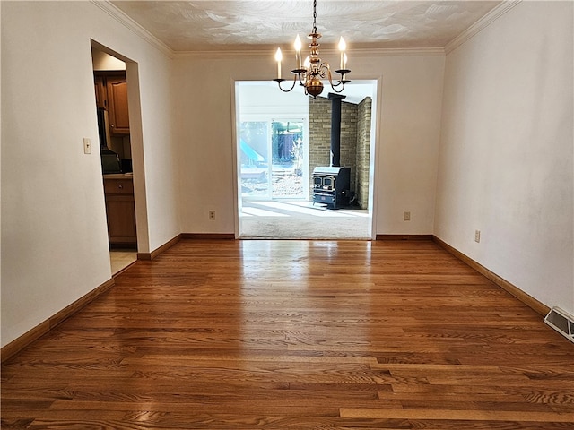 unfurnished dining area with a wood stove, ornamental molding, a chandelier, and dark wood-type flooring