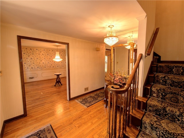 stairway with ornamental molding, wood-type flooring, and an inviting chandelier