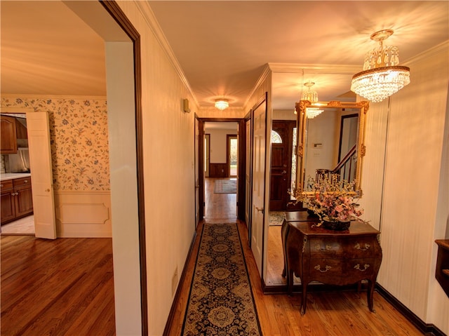 hallway with crown molding, wood-type flooring, and an inviting chandelier