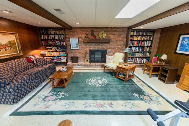 carpeted living room featuring a paneled ceiling, wooden walls, and a brick fireplace