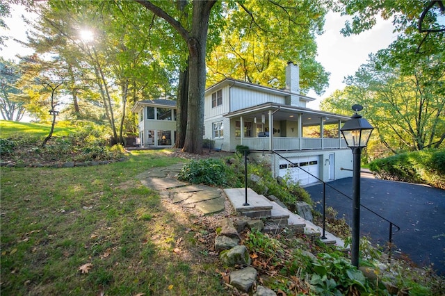 rear view of house with covered porch, a garage, and a lawn