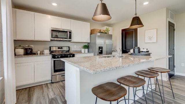 kitchen featuring sink, hanging light fixtures, appliances with stainless steel finishes, an island with sink, and white cabinets