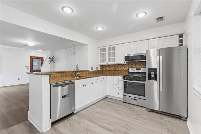 kitchen with kitchen peninsula, dark stone counters, white cabinets, appliances with stainless steel finishes, and light hardwood / wood-style floors