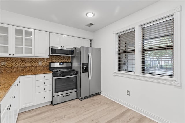 kitchen with stainless steel appliances, dark stone counters, light wood-type flooring, and white cabinets