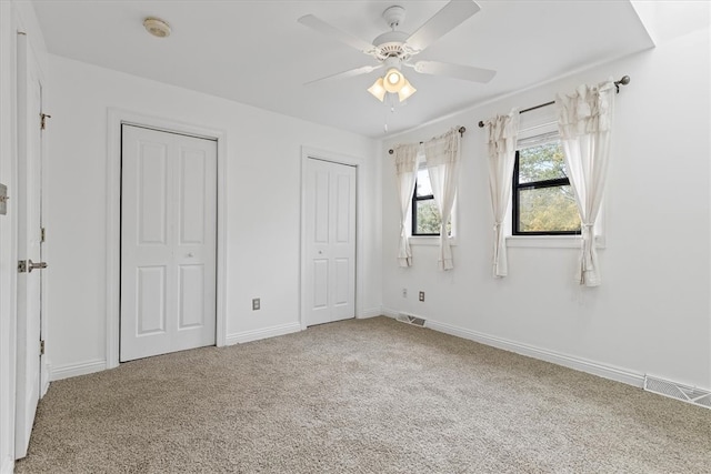 unfurnished bedroom featuring two closets, carpet floors, and ceiling fan