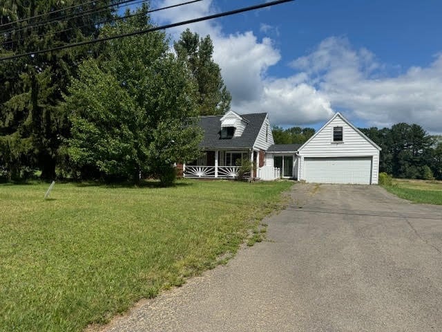 new england style home featuring a porch, a front lawn, and a garage