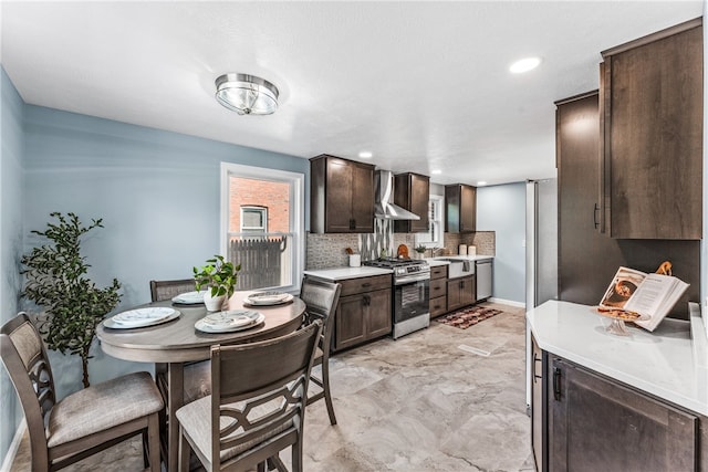 kitchen with appliances with stainless steel finishes, wall chimney range hood, dark brown cabinets, and backsplash