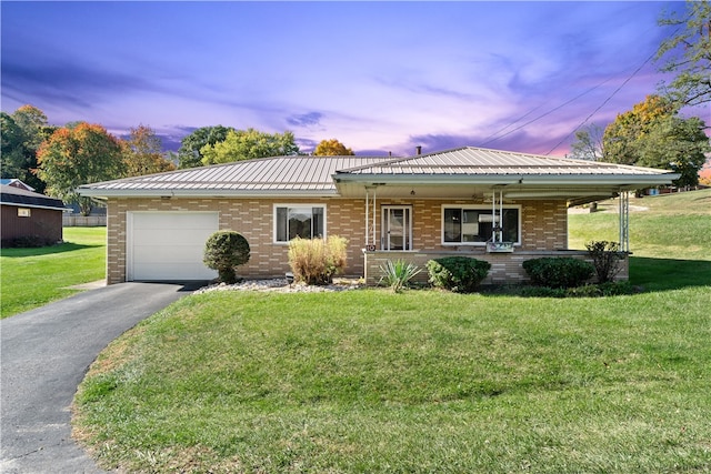 ranch-style house featuring aphalt driveway, brick siding, a yard, metal roof, and a garage