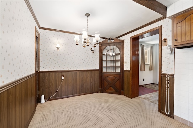 carpeted spare room with ornamental molding, a notable chandelier, and wood walls