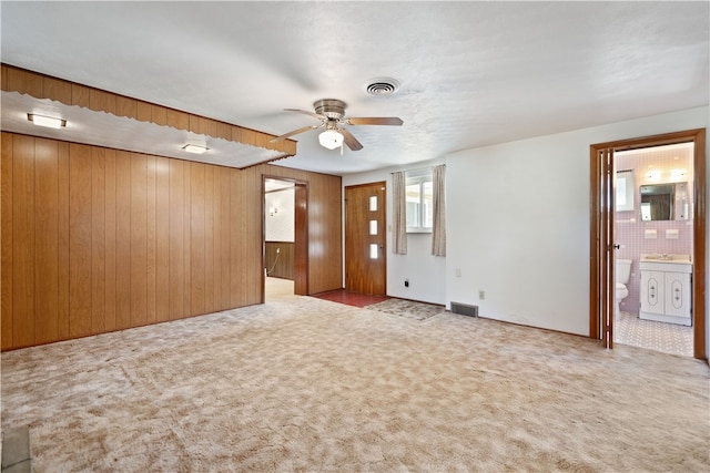 carpeted empty room with wood walls, sink, and ceiling fan