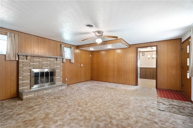 unfurnished living room with wooden walls, carpet flooring, plenty of natural light, and a brick fireplace