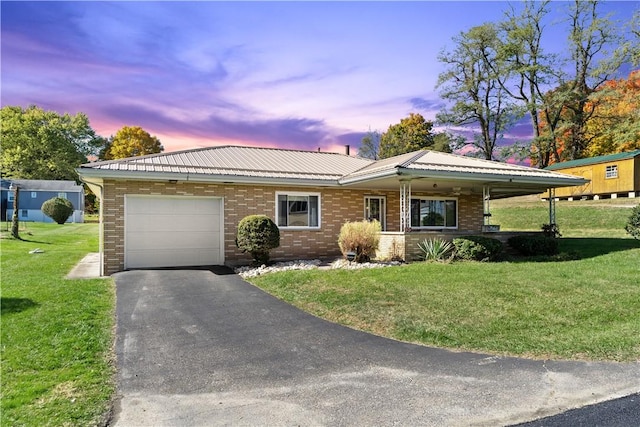 single story home with a garage, driveway, metal roof, a yard, and brick siding