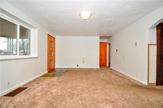 carpeted spare room featuring arched walkways, visible vents, and baseboards