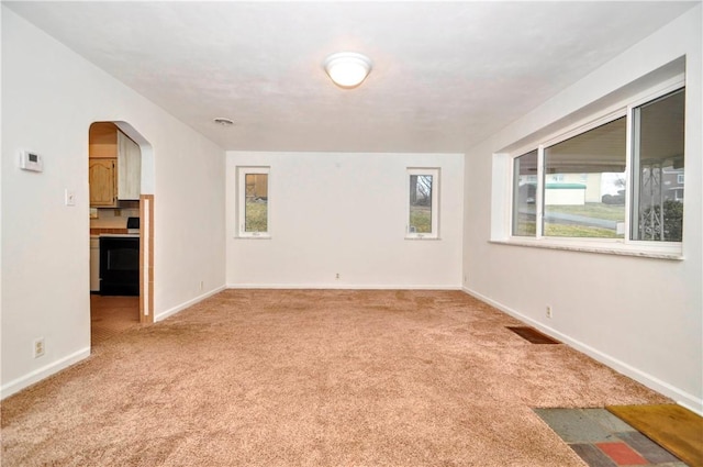 spare room with arched walkways, light carpet, visible vents, and baseboards