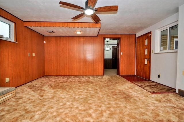 carpeted empty room featuring ceiling fan, wooden walls, and visible vents