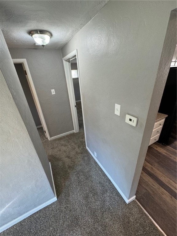 hall featuring dark carpet and a textured ceiling