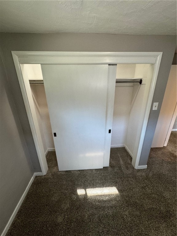 unfurnished bedroom with dark carpet, a textured ceiling, and a closet