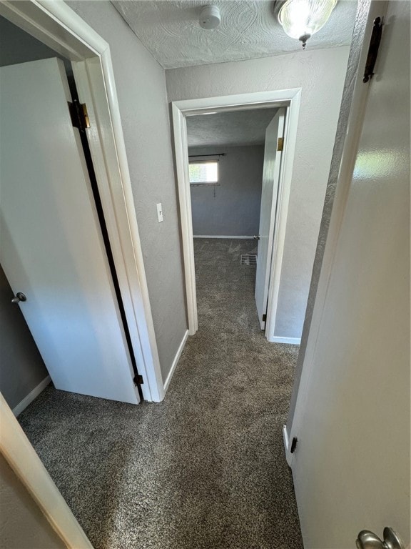 corridor featuring a textured ceiling and dark carpet