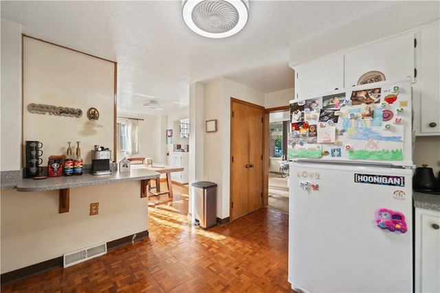 kitchen with white fridge, dark parquet floors, and white cabinets