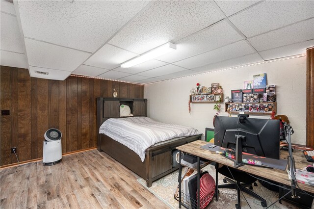 bedroom featuring wooden walls, a paneled ceiling, and light hardwood / wood-style floors