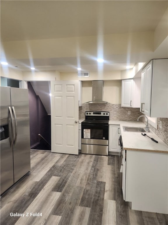 kitchen with sink, wall chimney exhaust hood, appliances with stainless steel finishes, white cabinetry, and wood-type flooring