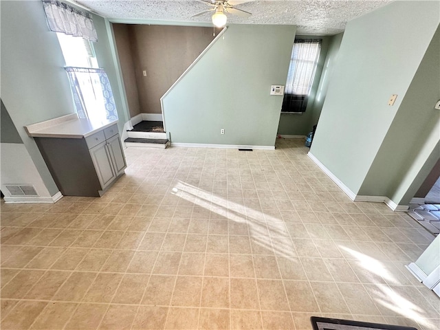 unfurnished living room with ceiling fan, a textured ceiling, and light tile patterned flooring