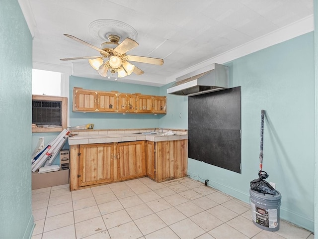 kitchen featuring ceiling fan, ornamental molding, light tile patterned floors, and tile counters