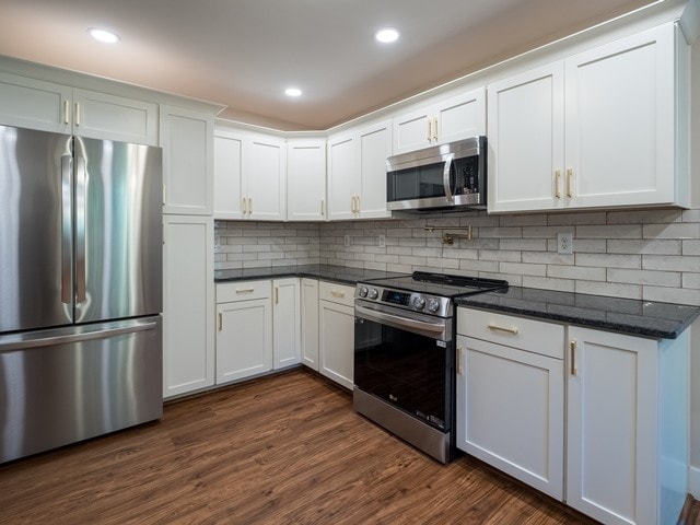 kitchen featuring dark hardwood / wood-style floors, white cabinets, stainless steel appliances, and dark stone counters