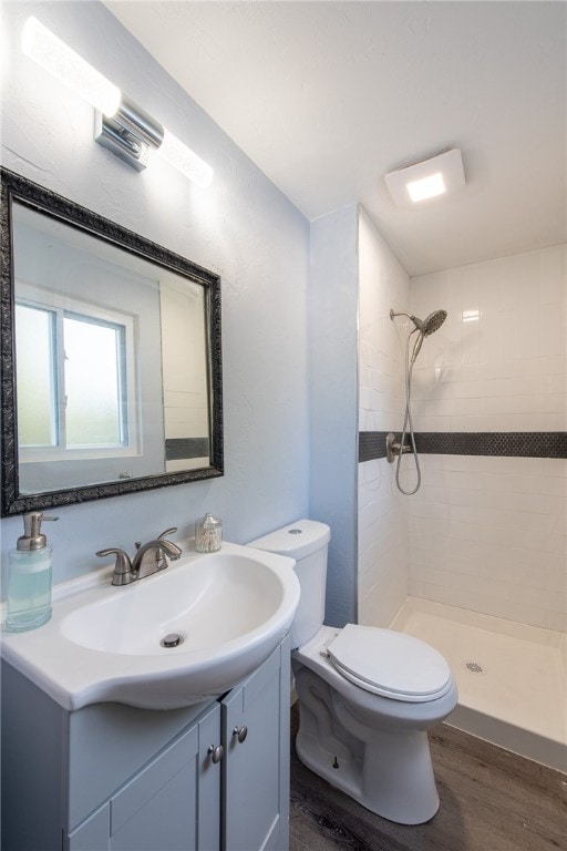 bathroom with vanity, hardwood / wood-style floors, tiled shower, and toilet