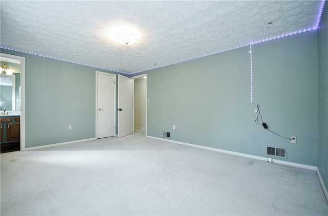 unfurnished bedroom featuring ensuite bath, light carpet, and a textured ceiling