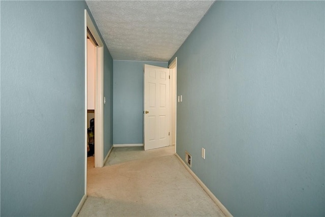 hallway with light colored carpet and a textured ceiling