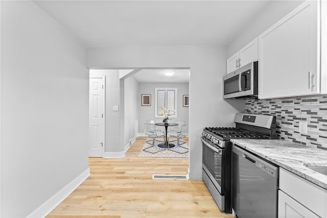 kitchen featuring light stone counters, backsplash, white cabinetry, light hardwood / wood-style floors, and stainless steel appliances