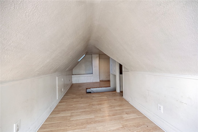 additional living space with vaulted ceiling, light hardwood / wood-style flooring, and a textured ceiling