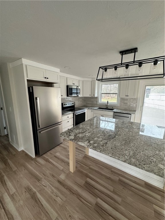 kitchen with appliances with stainless steel finishes, light stone counters, sink, hardwood / wood-style floors, and white cabinetry